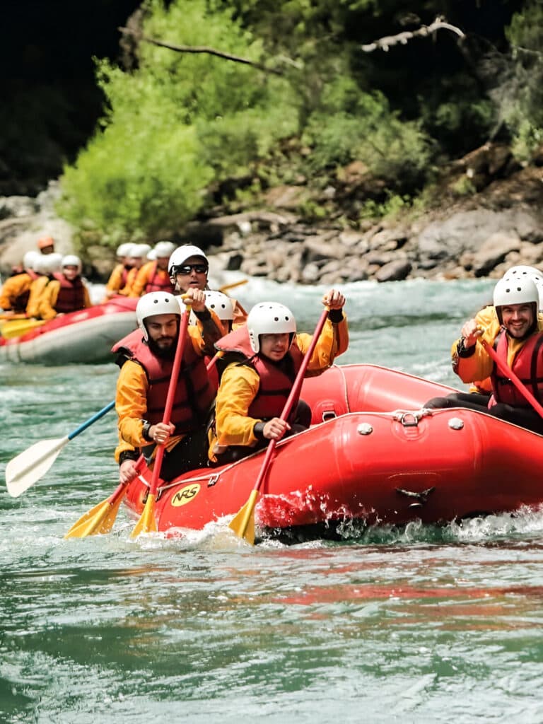 Dos botes de rafting bajan juntos el río Manso entre el bosque, con la tripulación remando